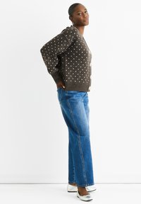 Brown knitted cardigan with white polka dots, button front, oversized fit. Paired with light blue flared jeans and silver flat shoes.
