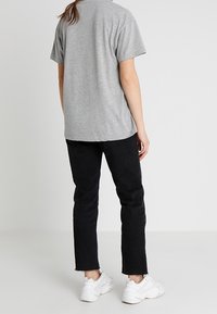 Camiseta de algodón gris con mangas cortas, combinada con jeans de mezclilla negra. Las zapatillas son blancas y tienen un diseño grueso. El dobladillo de los jeans está deshilachado.