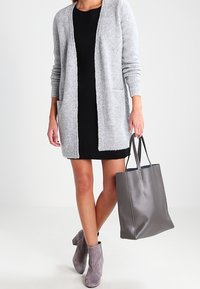 Grå stickad cardigan med öppen front, bärs över en svart klänning; en grå läderhandväska och grå ankelskor fullbordar looken.