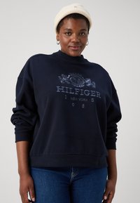 Granatowy sweatshirt z okrągłym dekoltem, zdobiony jasnoniebieskim graficznym logo na piersi; miękka tkanina i ściągacze przy rękawach.