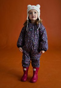 Fluorowy, granatowy wodoodporny kombinezon zimowy w kwiatowy wzór z elastycznymi mankietami i metką JoJo, w połączeniu z jasnoróżowymi gumowymi butami oraz czapką z motywem misia.