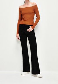 Schulterfreier, gerippter Pullover in verbranntem Orange, kombiniert mit hochtaillierten, schwarzen Schlaghosen und weißen Sneakers.
