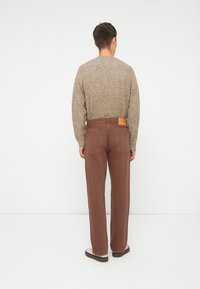 Pantaloni marroni a vita alta con taglio dritto, caratterizzati da una toppa in pelle sul retro e un maglione in maglia beige strutturata.