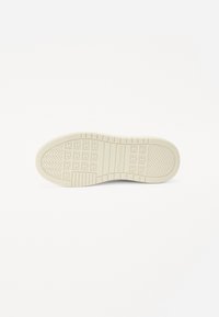 Batų pado medžiaga - off-white gumos su tekstūruotais sukibimo raštais, kuriuose yra stačiakampių ir apvalių formų, užtikrinančių sukibimą ir ilgaamžiškumą.