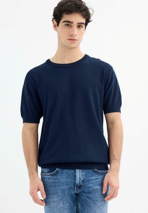 Suéter de manga corta en azul marino con un patrón texturizado, cuello redondo y puños y dobladillo acanalados. Combinado con jeans de color azul claro.