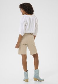 Beige shorts i bomullsmix med bakfickor. Kombineras med en vit, strukturerad blus med lång ärm och blå cowboyboots.
