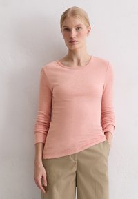 Langärmliges, Rundhalsoberteil in Hellrosa, gefertigt aus einem weichen, strukturierten Stoff. Auffälliges, siebgedrucktes Branding auf der Brust.