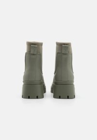 Botas de tobillo verdes hechas de material suave, con un tacón grueso, punta redonda y detalles de costura a lo largo de la parte superior y lateral.