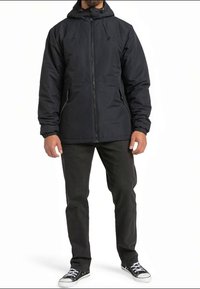 Casaco preto com fecho e capuz, punhos elásticos e dois bolsos frontais. Combinado com calças pretas e sapatilhas pretas. Acabamento liso e mate.