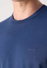 Gros plan d'une personne portant un t-shirt bleu à col rond avec le mot "BOSS" imprimé sur la poitrine.