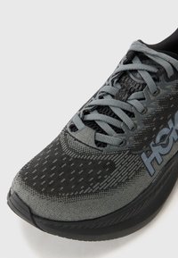 Chaussure de course légère avec une tige en maille grise, des accents noirs, des motifs texturés et des lacets gris. Elle présente un bout arrondi et une semelle rembourrée.