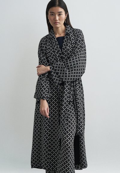 Langer schwarzer Mantel mit einem weißen geometrischen Muster, breiten Ärmeln, einem Bindegürtel und einem fließenden Design. Strukturierter Stoff verleiht Tiefe.