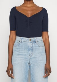 Námořnický modrý body s krátkým rukávem, v dekoltu tvaru V a shromážděním uprostřed. V kombinaci s světle modrými džíny s vysokým pasem.