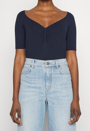 Marineblå kortærmet bodysuit med V-hals og samlet detalje i midten. Kombineret med lyse vasket højtaljede jeans.