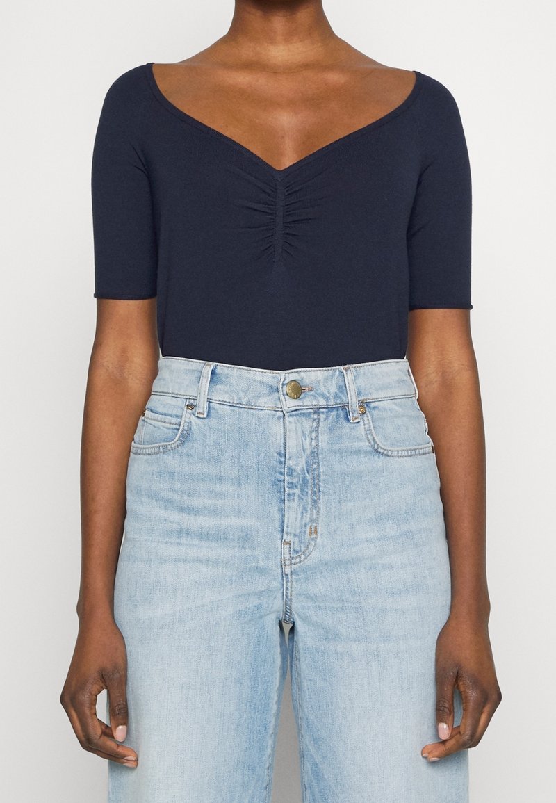 Námořnický modrý body s krátkým rukávem, v dekoltu tvaru V a shromážděním uprostřed. V kombinaci s světle modrými džíny s vysokým pasem.