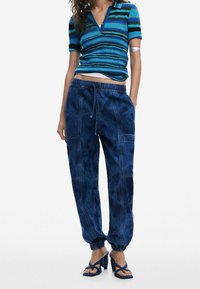 Polo à rayures bleues côtelées à manches courtes, associé à un pantalon ample bleu foncé avec taille et poignets élastiques.