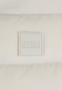 Hvid dunjakke stof med quiltet struktur; har en markant syet logo patch "URBAN CLASSICS" i firkantet format.