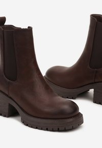 Bottines en cuir marron avec des panneaux élastiques sur les côtés, un bout rond et un talon texturé, présentant une surface lisse et une semelle robuste.