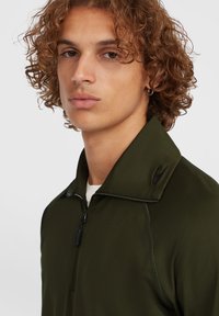 Giacca verde con zip e colletto alto, realizzata in tessuto liscio. Presenta dettagli di cucitura sottili e un piccolo logo sul colletto.
