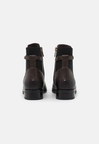 Bottines en cuir marron avec des panneaux en tissu noir extensible, des fermetures à glissière, des talons plats, et un petit logo à l'arrière.