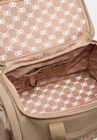 Zaino beige con un interno a fantasie rosa che presenta disegni circolari bianchi. Include una tasca in rete e una chiusura con zip.