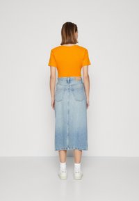 Oranžové tričko s krátkým rukávem, spárované s světle modrou džínovou midi sukňí. Bílé tenisky s ponožkovými akcenty dotvářejí celý outfit.