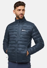 Marineblaue Steppjacke mit einem gesteppten Design, hohem Kragen, Frontreißverschluss und Seitentaschen. Mit einem Logo auf der Brust und verstellbarem Saum.