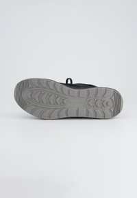 Zwarte sneaker met een gestructureerde grijze rubberen zool met een zigzagpatroon, tractiedots en een trekband aan de hiel voor gemakkelijk aantrekken.