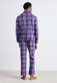 Pijamas de cuadros rojos y azules hechos de una tela suave, que incluyen una camisa de botones de manga larga y pantalones a juego con un ajuste cómodo.