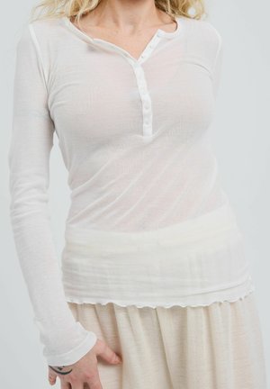White long-sleeve henley shirt with a button placket and soft, lightweight fabric; paired with a beige, textured, flowing skirt.
