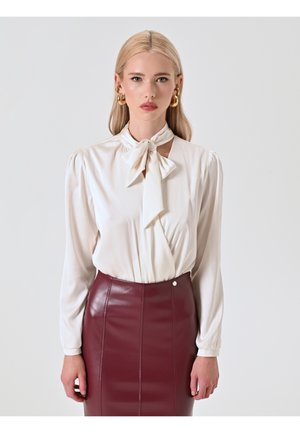 Blusa crema con un fiocco annodato al collo, maniche lunghe con spalle plissettate, abbinata a una gonna a matita in pelle bordeaux.