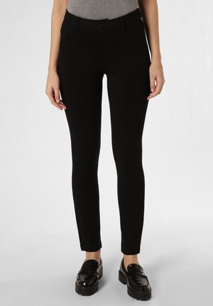 Pantalons noirs ajustés en tissu extensible, présentant des poches, une taille mi-haute et une texture lisse, associés à des mocassins noirs.