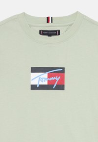 Mintgrünes T-Shirt mit Rundhalsausschnitt. Verfügt über ein grafisches Logo in Blau, Rot und Schwarz auf einem weißen Hintergrund. Weicher Baumwollstoff.