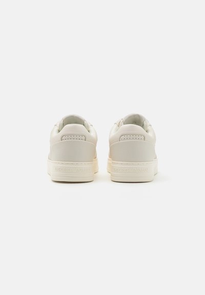 Baskets en cuir blanc avec une texture lisse, présentant un design basse, un bout rond et un logo en relief sur le talon.