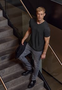 Zwarte V-hals T-shirt gecombineerd met grijze slim fit jeans en zwarte leren enkellaarsjes, met een blazer van textuurstof over één arm gedrapeerd.