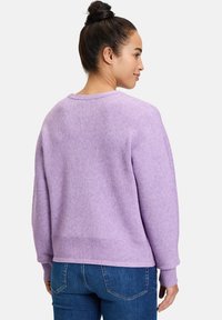 Lila, gerippter Pullover mit langen Ärmeln, einem runden Ausschnitt und einer strukturierten Oberfläche. Kombiniert mit blauen Jeans.