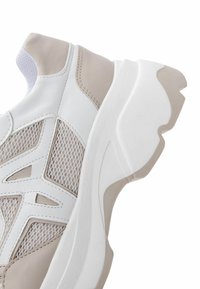 White athletic shoes with beige accents, featuring mesh panels and a chunky sole design. Smooth leather and textured mesh materials used.