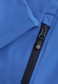 Blått tyg med en slät yta, utrustat med en dragkedja och en kardborreflik. Dragkedjan är svart med en mönstrad dragring, placerad på en mörkare panel.