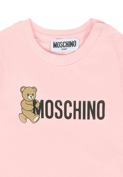 Maglietta baby rosa con una grafica di orsetto che abbraccia la lettera "M" e "MOSCHINO" stampato in bold nero sul petto.
