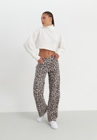 Sweater branco encurtado com gola alta, combinado com calças largas de padrão leopardo. Modelo usa ténis brancos. Texturas suaves, caimento descontraído.