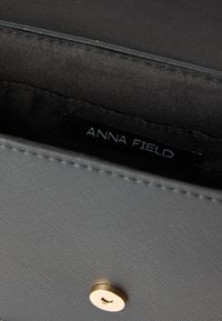 Κοντινή λήψη εσωτερικού μαύρης υφασμάτινης τσάντας με μαγνητικό κούμπωμα και ραμμένη ετικέτα υφάσματος "ANNA FIELD".