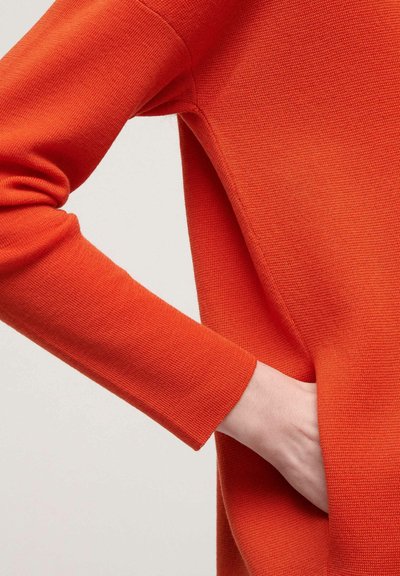 Orange knit sweater with long sleeves, featuring a textured fabric and a side pocket, emphasizing a simple, relaxed design.