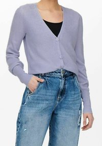 Ljus lavendelfärgad ribbad kofta med V-ringning, utrustad med två framknappar och långa ärmar, ihop med högmidjade slitna blå jeans.