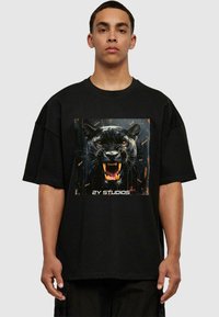 Fekete, túlméretezett póló, középre nyomtatva egy ordító fekete párduc grafikájával, narancssárga kiegészítőkkel, puha anyagon.