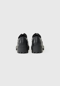 Chaussures en cuir noir avec un bout rond, une semelle en caoutchouc épaisse et des accents perforés décoratifs sur le talon et les côtés.