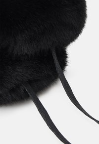 Bolso de piel sintética negra con forma redonda, textura suave y cierre de cordón negro. El pelaje es denso y brillante.