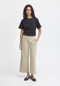 T-shirt noir en coton associé à un pantalon large à carreaux clairs et des ballerines noires. La tenue présente un design simple et une coupe décontractée.