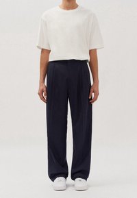 Vit oversized t-shirt i kombination med marinblå högmidjade pliébyxor, bärs med vita sneakers. Enkel design, mjukt tyg och avslappnad passform.