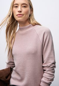 Pull en tricot rose clair avec un col montant, des détails côtelés et des manches longues, offrant une coupe décontractée et une texture douce.