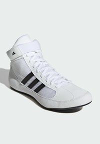 White athletic shoe with mesh and leather panels, featuring black accent stripes and a high-top design with a Velcro strap for support.